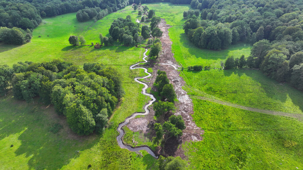 Ett foto som visar ett landskap uppifrån med ett meandrande vattendrag, öppna gräsmarker och lövträdsgungar.