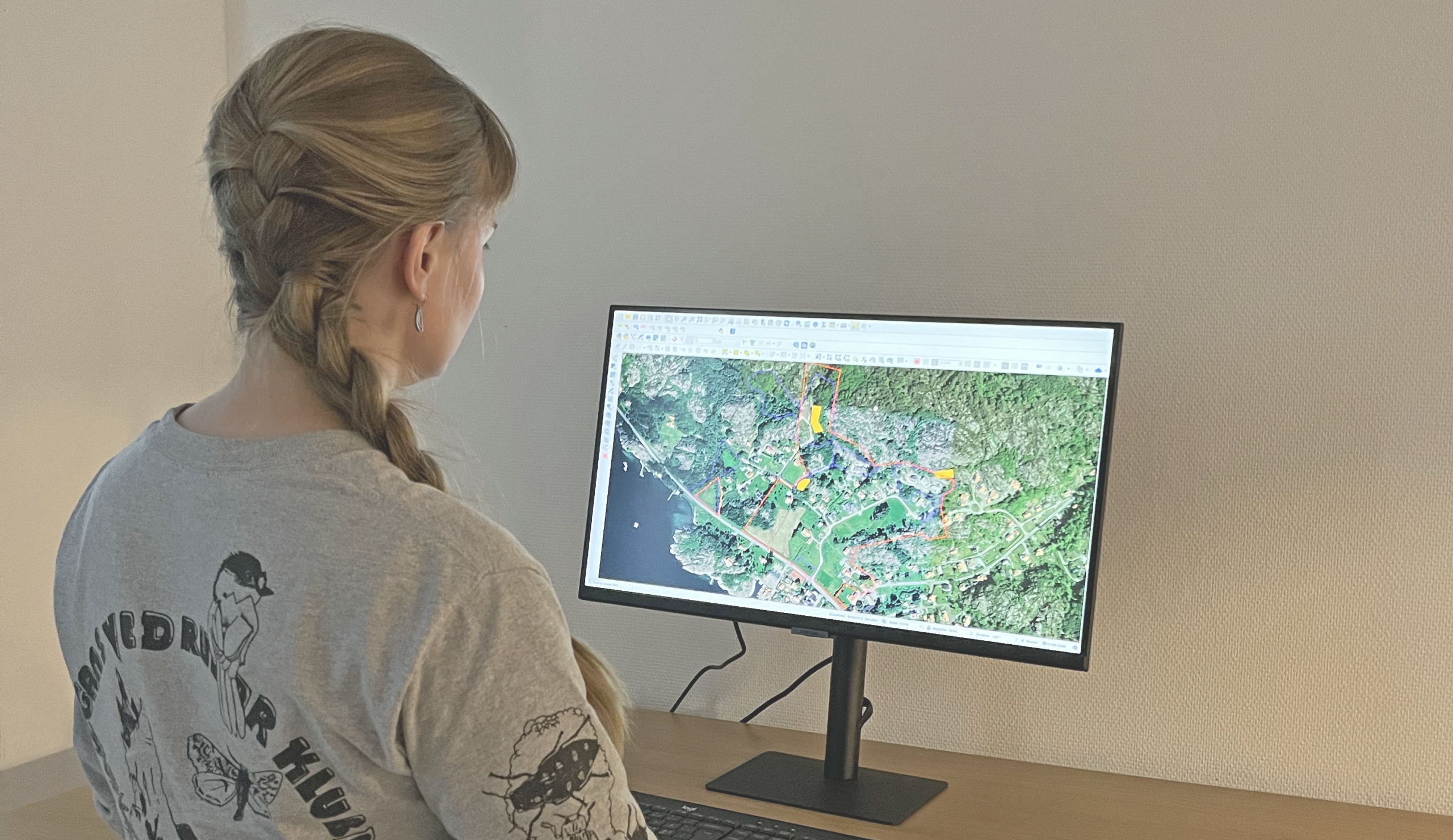 Ett foto som visar en person som tittar på en datorskäm, på vilken en karta med olikafärgade ytor visas.