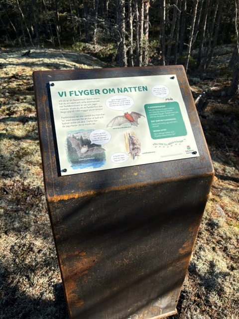 Foto av en skylt som är monterad på ett lutande skyltställ som står ute i naturen.